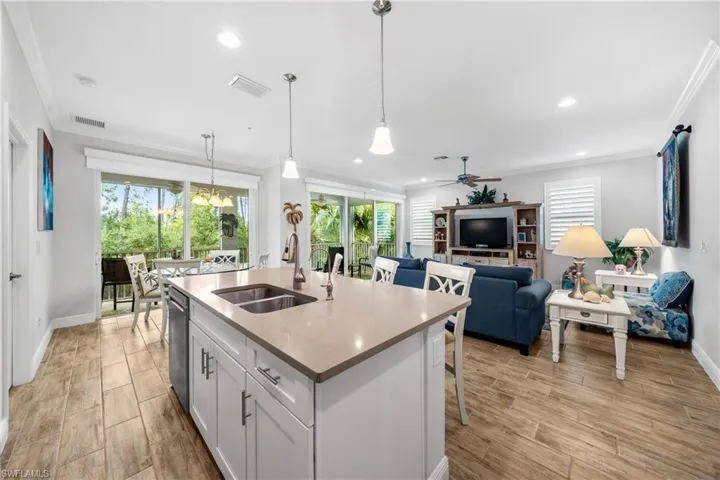 Open concept living area featuring a kitchen island with dual sinks, wood-finish flooring, recessed lighting, and a screened lanai