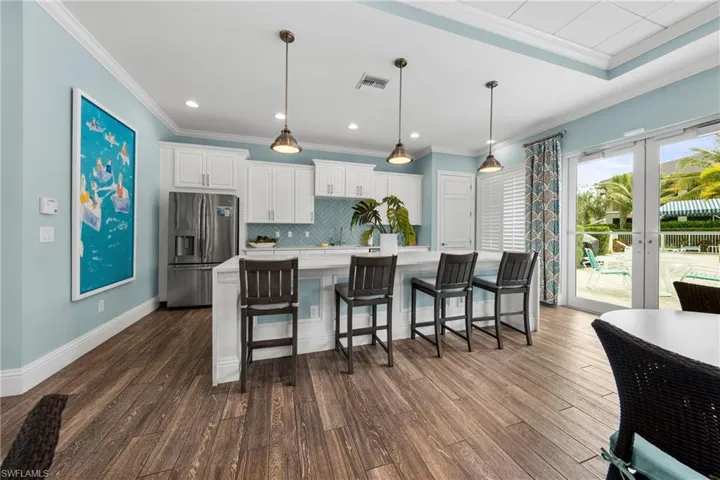 Kitchen area featuring a central island with seating for four, white shaker-style cabinetry, stainless steel appliances, wood-finish flooring, and direct access to an outdoor patio with a pool