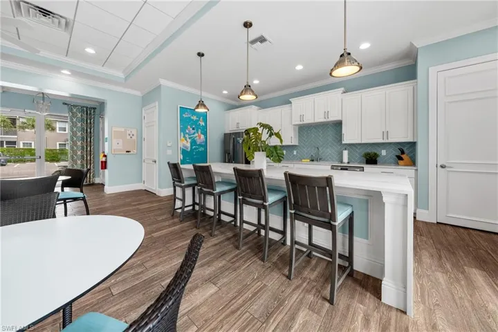 Open-concept common area featuring a full kitchen with white cabinetry, a herringbone tile backsplash, and a large central island with seating for four