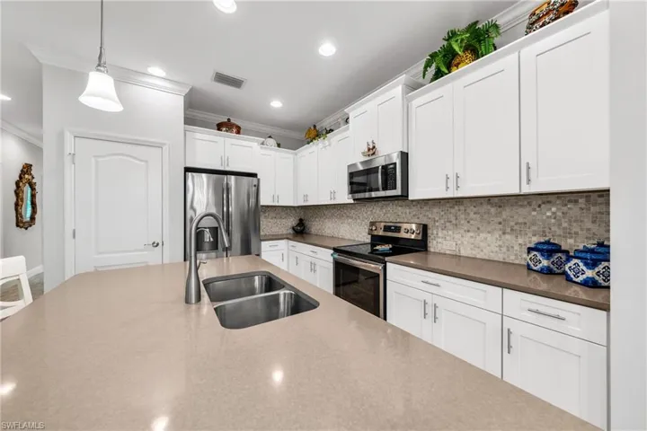 Spacious kitchen featuring a large island with an undermount double basin sink, stainless steel appliances, white shaker cabinetry, mosaic tile backsplash, and recessed lighting