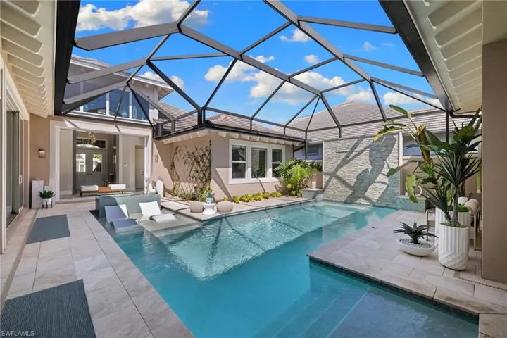 Screened-in outdoor living space featuring a rectangular pool, integrated sun shelf, stone-finish water feature, and light-tone tile flooring