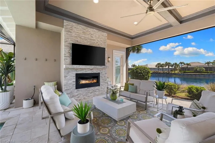 Covered outdoor living space featuring a stacked stone fireplace with an integrated electric firebox, a ceiling fan, coffered ceiling, and large format tile flooring