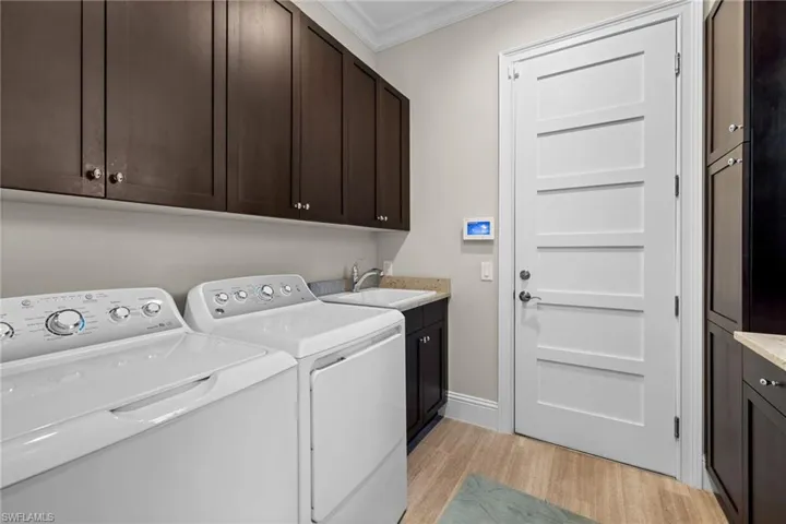 Laundry area featuring wood-finish flooring, dark wood cabinetry, and a granite-topped utility sink with a chrome faucet