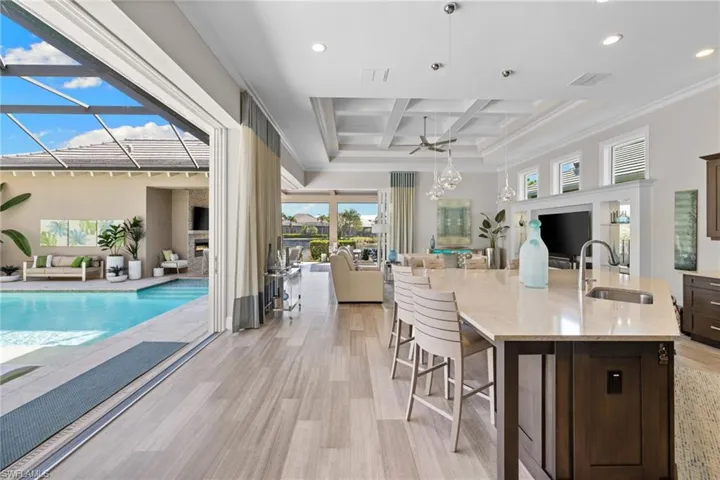 Expansive open-concept interior featuring wood-finish flooring, a coffered ceiling, and large sliding glass doors opening to a screened lanai with a swimming pool