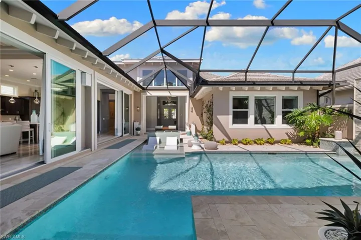Screened outdoor living space featuring a rectangular swimming pool with integrated tanning ledge, stone paver decking, multiple sets of sliding glass doors, and recessed lighting