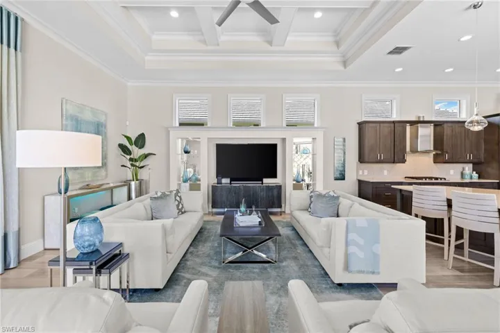 Open-concept living area featuring a coffered ceiling with recessed lighting, an integrated kitchen with dark wood cabinetry and a stainless steel range hood, and light wood-finish flooring