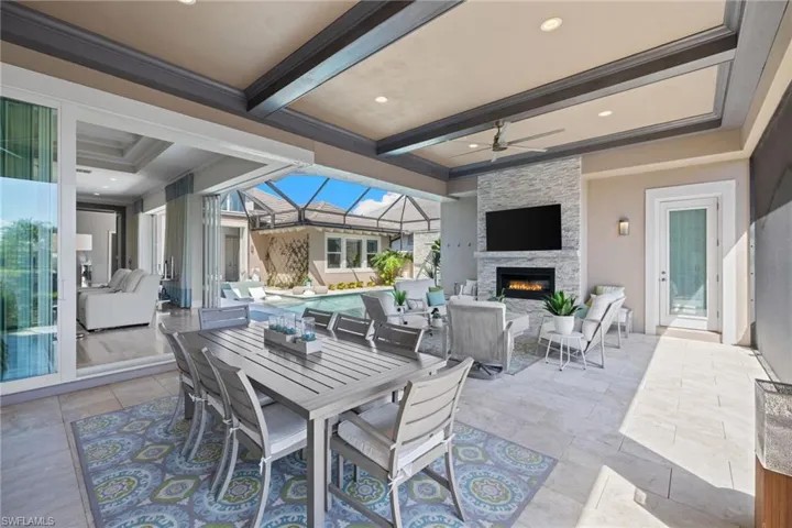 Expansive covered patio featuring a large dining area, a built-in fireplace with a stacked stone facade, and a recessed ceiling with exposed beams