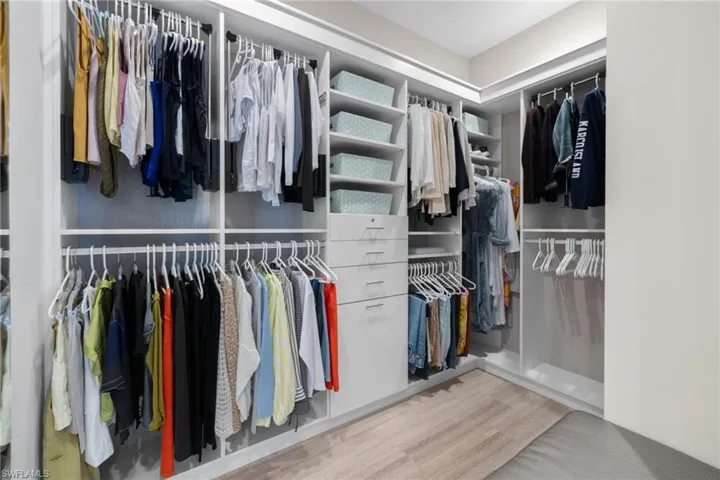 Walk-in closet #1, custom closet system featuring multiple hanging rods, open shelving, integrated drawers, and wood-finish flooring
