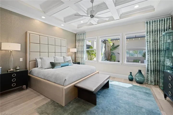 Primary bedroom #1, featuring coffered ceiling featuring a ceiling fan and recessed lighting, wood-finish flooring, and multiple windows providing natural illumination