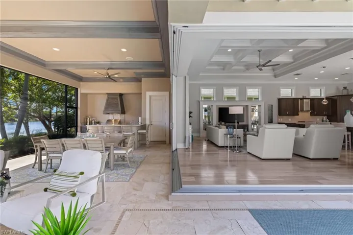 Expansive indoor-outdoor living area featuring retractable glass doors, coffered ceilings, and a screened lanai with a built-in outdoor kitchen