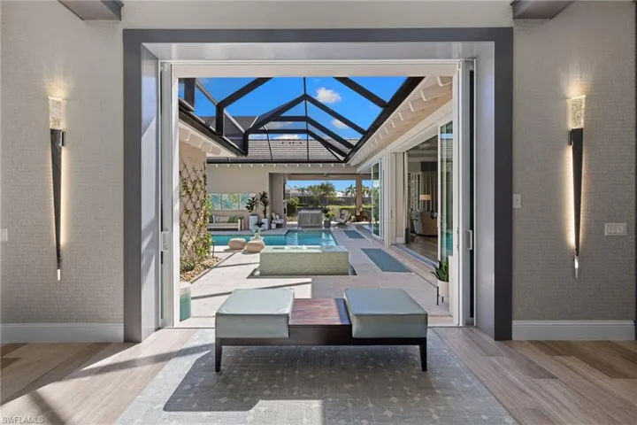 Entry way hallway facing expansive outdoor living area featuring a screened-in pool enclosure, integrated pool with a spa, and a stone-look patio