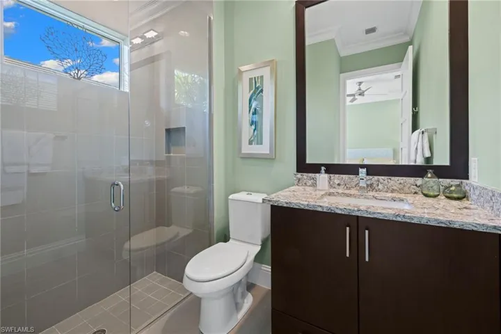 Bathroom #2, featuring a glass-enclosed shower with tile surround, built-in shower niche, a granite countertop vanity with integrated sink, and a framed mirror