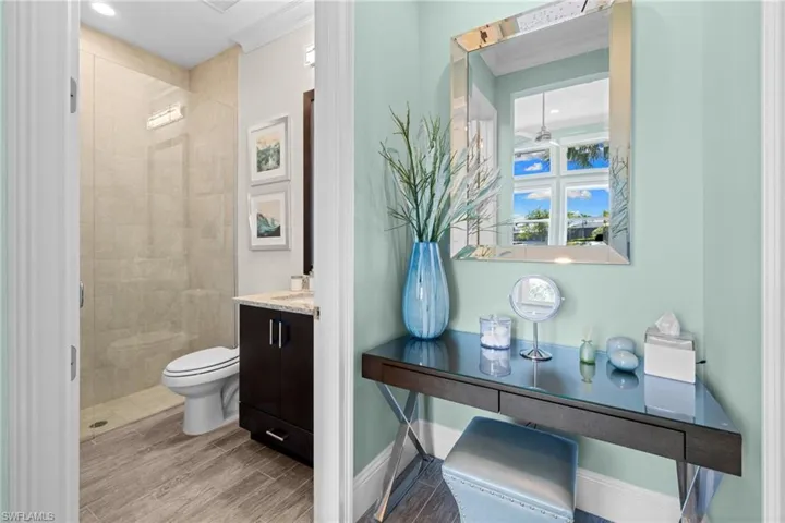 Bathroom #3, featuring a beveled mirror, dark wood-finish desk with a glass top, and a light blue wall color