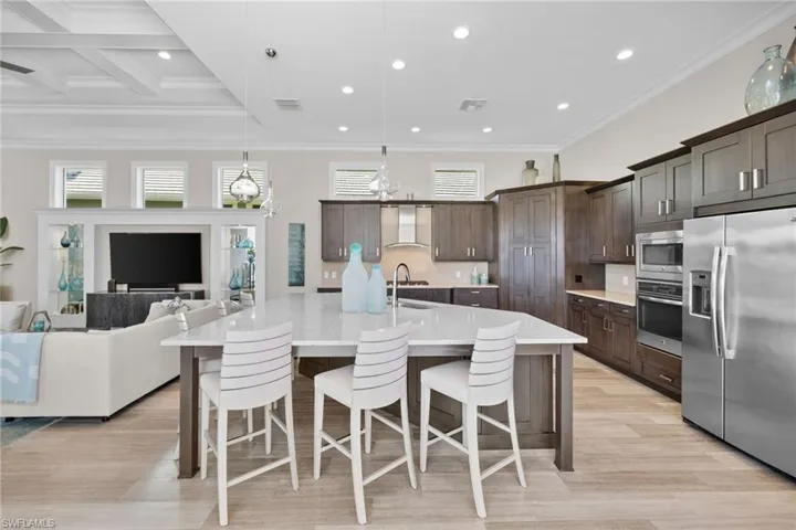 Open-concept kitchen featuring a large island with seating, stainless steel appliances, extensive cabinetry, and wood-finish flooring