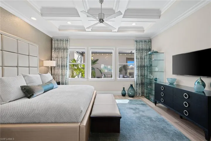 Primary bedroom #1, featuring tray ceiling with recessed lighting and a ceiling fan, wall-mounted television, wood-finish flooring, and multiple windows