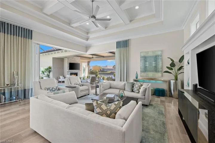 Expansive living area featuring coffered ceilings with recessed lighting, wood-finish flooring, and large sliding glass doors