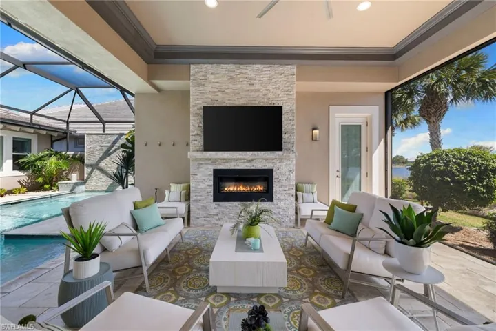 Screened outdoor living area featuring a stacked stone fireplace with an integrated television, direct pool access, and waterfront scenery