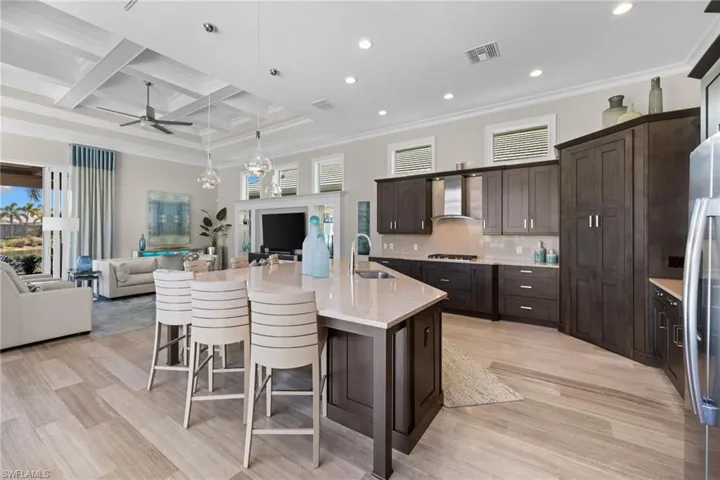 Open-concept kitchen and living area featuring wood-finish flooring, a coffered ceiling with recessed lighting, and a kitchen island with pendant lighting