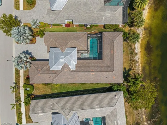 Overhead view of a residential property featuring a screened swimming pool, tile roofing, and a paved driveway