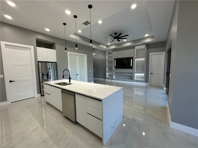 Kitchen featuring pendant lighting, sink, stainless steel appliances, white cabinets, and a large island with sink