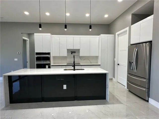 Kitchen with white cabinetry, hanging light fixtures, stainless steel appliances, light stone countertops, and a large island with sink