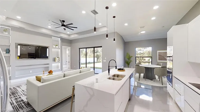 Kitchen with light stone counters, decorative light fixtures, an island with sink, and white cabinets