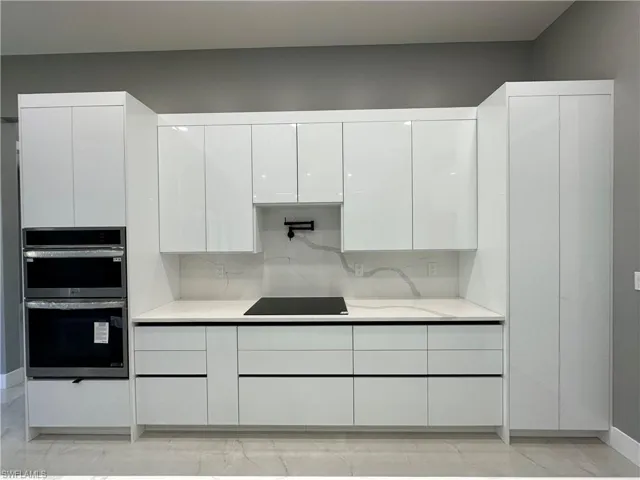 Kitchen with white cabinetry, light stone counters, black electric cooktop, stainless steel double oven, and decorative backsplash