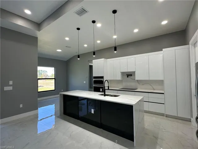 Kitchen featuring decorative light fixtures, an island with sink, sink, white cabinets, and black electric cooktop