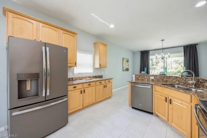 Kitchen featuring light brown cabinets, stainless steel appliances, decorative light fixtures, light tile floors, and sink
