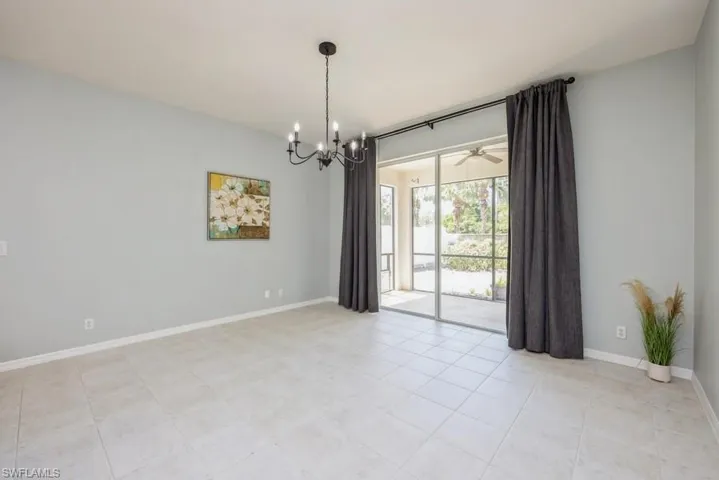 Tiled empty room featuring ceiling fan with notable chandelier