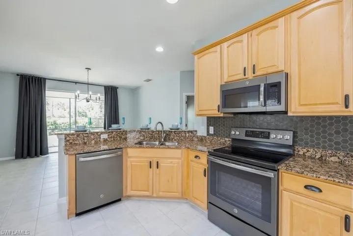 Kitchen with kitchen peninsula, light tile flooring, backsplash, sink, and appliances with stainless steel finishes