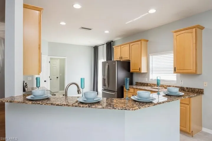 Kitchen with stone countertops, light brown cabinetry, stainless steel fridge with ice dispenser, and kitchen peninsula