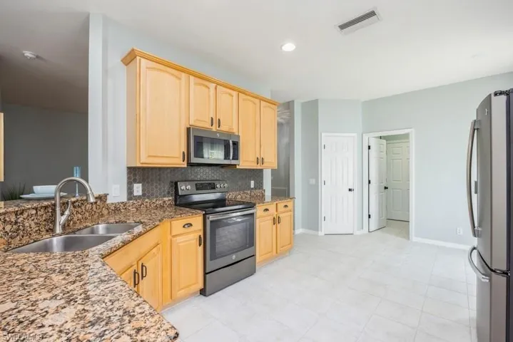 Kitchen featuring appliances with stainless steel finishes, sink, backsplash, and light tile floors