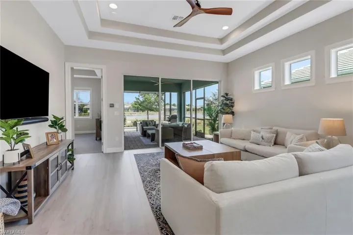 Living room with a tray ceiling, ceiling fan, and light wood-style flooring