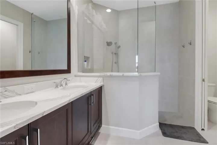 Bathroom with a walk in shower, tile patterned flooring, toilet, baseboards, and double vanity