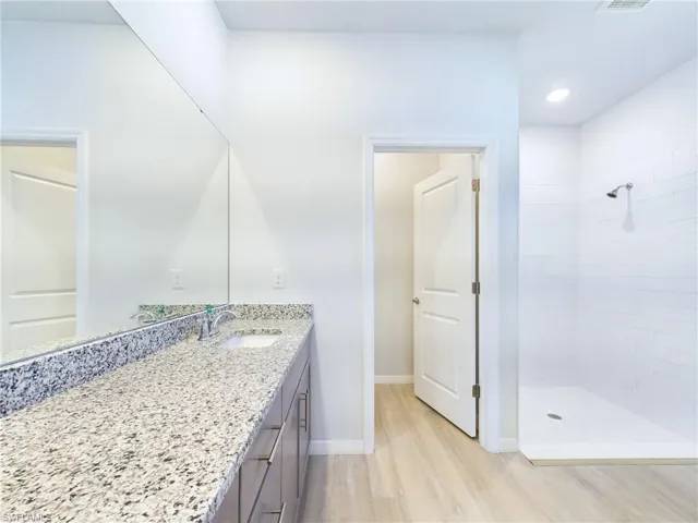 Bathroom with tiled shower, vanity, and wood-type flooring
