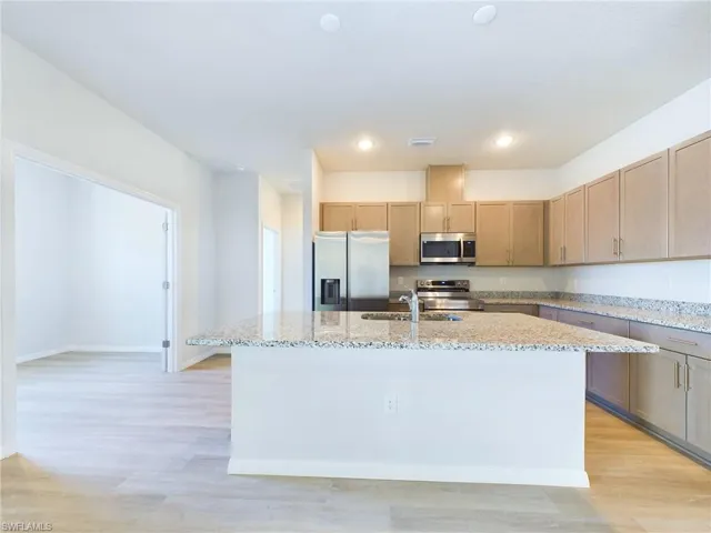 Kitchen featuring light stone counters, stainless steel appliances, a center island with sink, and light hardwood / wood-style flooring
