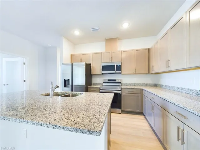 Kitchen featuring light hardwood / wood-style flooring, light stone countertops, stainless steel appliances, sink, and an island with sink