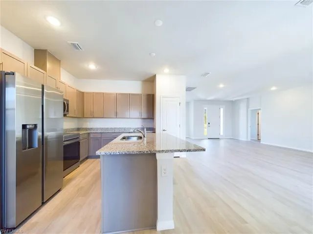 Kitchen with light stone counters, stainless steel appliances, light hardwood / wood-style floors, sink, and a kitchen island with sink