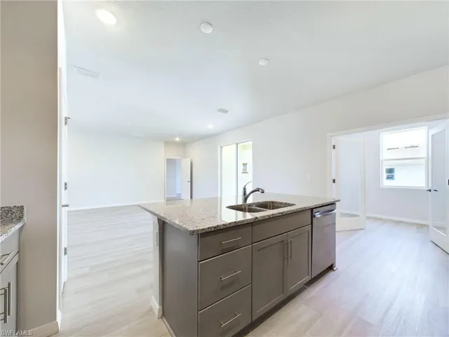 Kitchen with dishwasher, light hardwood / wood-style floors, an island with sink, sink, and light stone counters