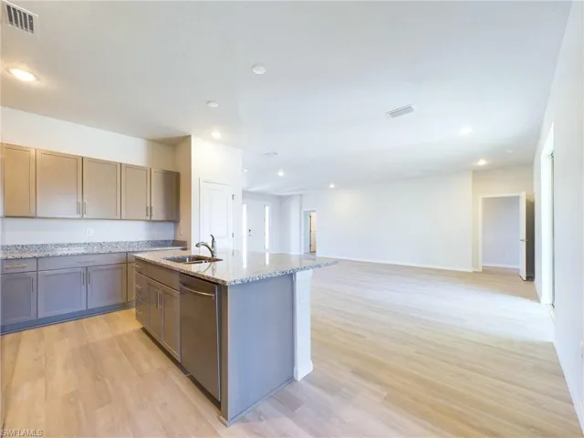 Kitchen featuring dishwasher, light hardwood / wood-style flooring, light stone counters, sink, and a kitchen island with sink
