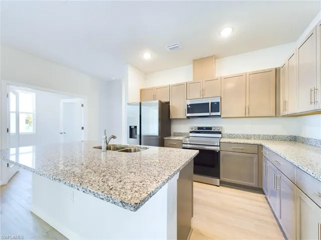 Kitchen featuring light stone countertops, light hardwood / wood-style flooring, a kitchen island with sink, stainless steel appliances, and sink