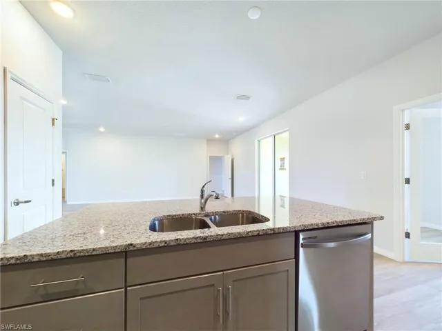 Kitchen with light hardwood / wood-style flooring, an island with sink, sink, light stone countertops, and stainless steel dishwasher