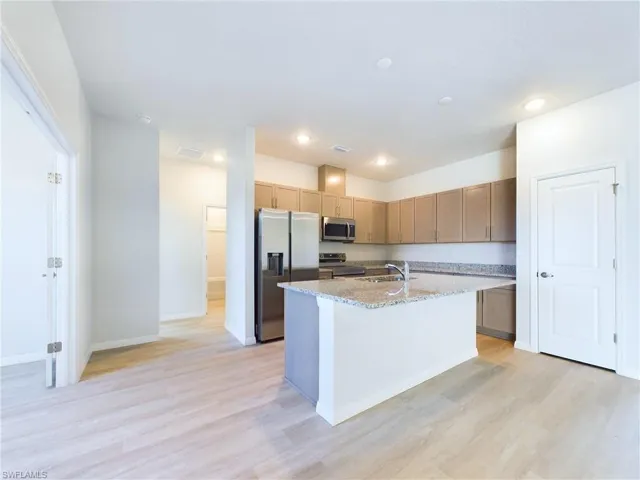 Kitchen with light wood-type flooring, stainless steel appliances, an island with sink, light stone countertops, and sink
