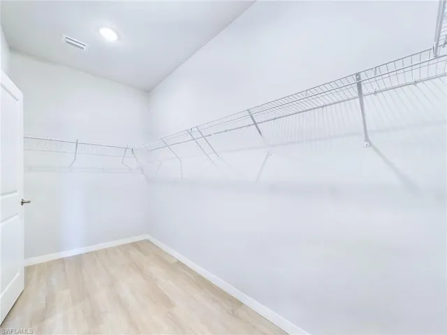 Walk in closet with light hardwood / wood-style flooring