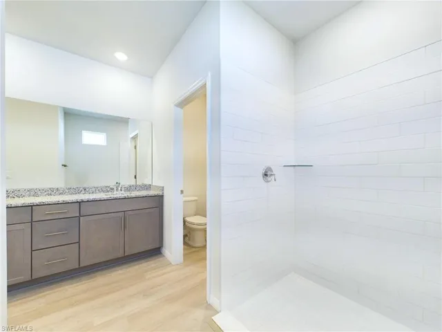 Bathroom featuring vanity, toilet, wood-type flooring, and a tile shower