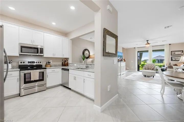 Kitchen featuring white cabinetry, light tile patterned floors, light stone counters, ceiling fan, and appliances with stainless steel finishes