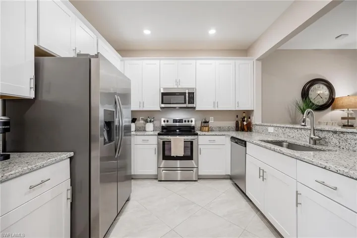 Kitchen with appliances with stainless steel finishes, light tile patterned floors, white cabinetry, and sink