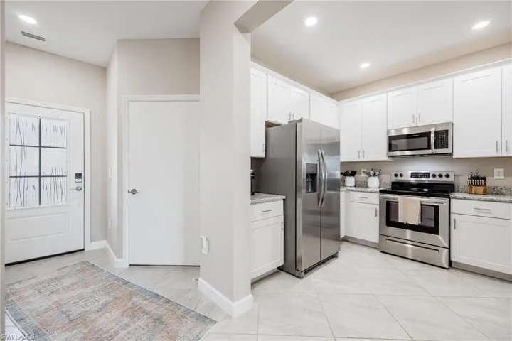 Kitchen featuring white cabinetry, light tile patterned flooring, stainless steel appliances, and light stone countertops