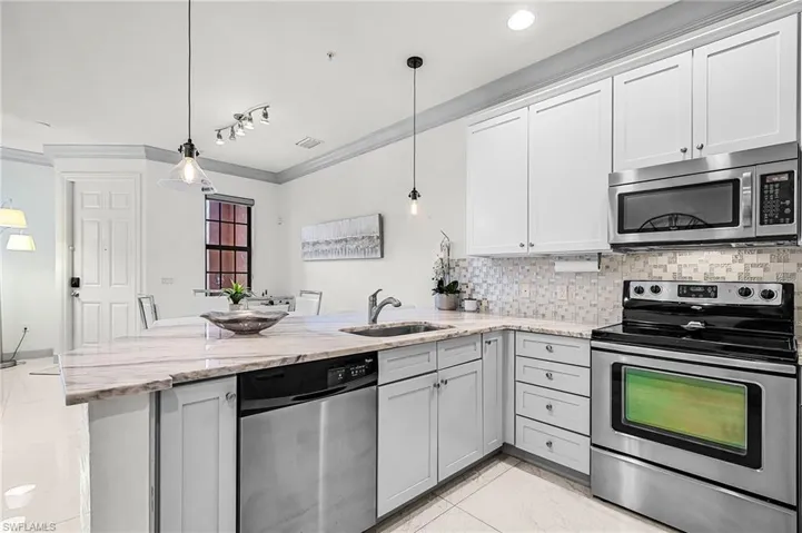 Kitchen with stainless steel appliances, decorative backsplash, light stone countertops, crown molding, and a peninsula
